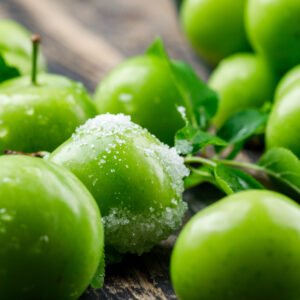 salty green plums with leaves on wooden background, close up.