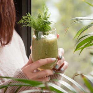 woman holding green detox smoothie with dills by window